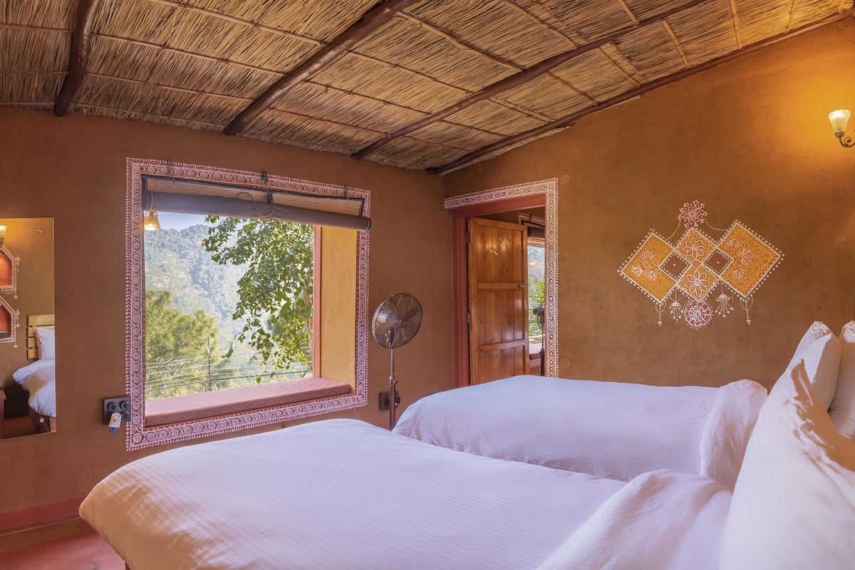 Una habitación con techo de paja, un ventanal con vistas a la vegetación, una cama con ropa blanca y un diseño decorativo en la pared.