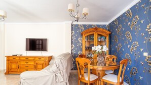 Una sala de estar con sofá, mesa de comedor con sillas, televisor y mueble.