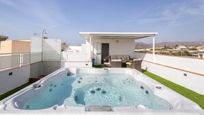 Una terraza con jacuzzi, asientos exteriores y vistas a la ciudad.