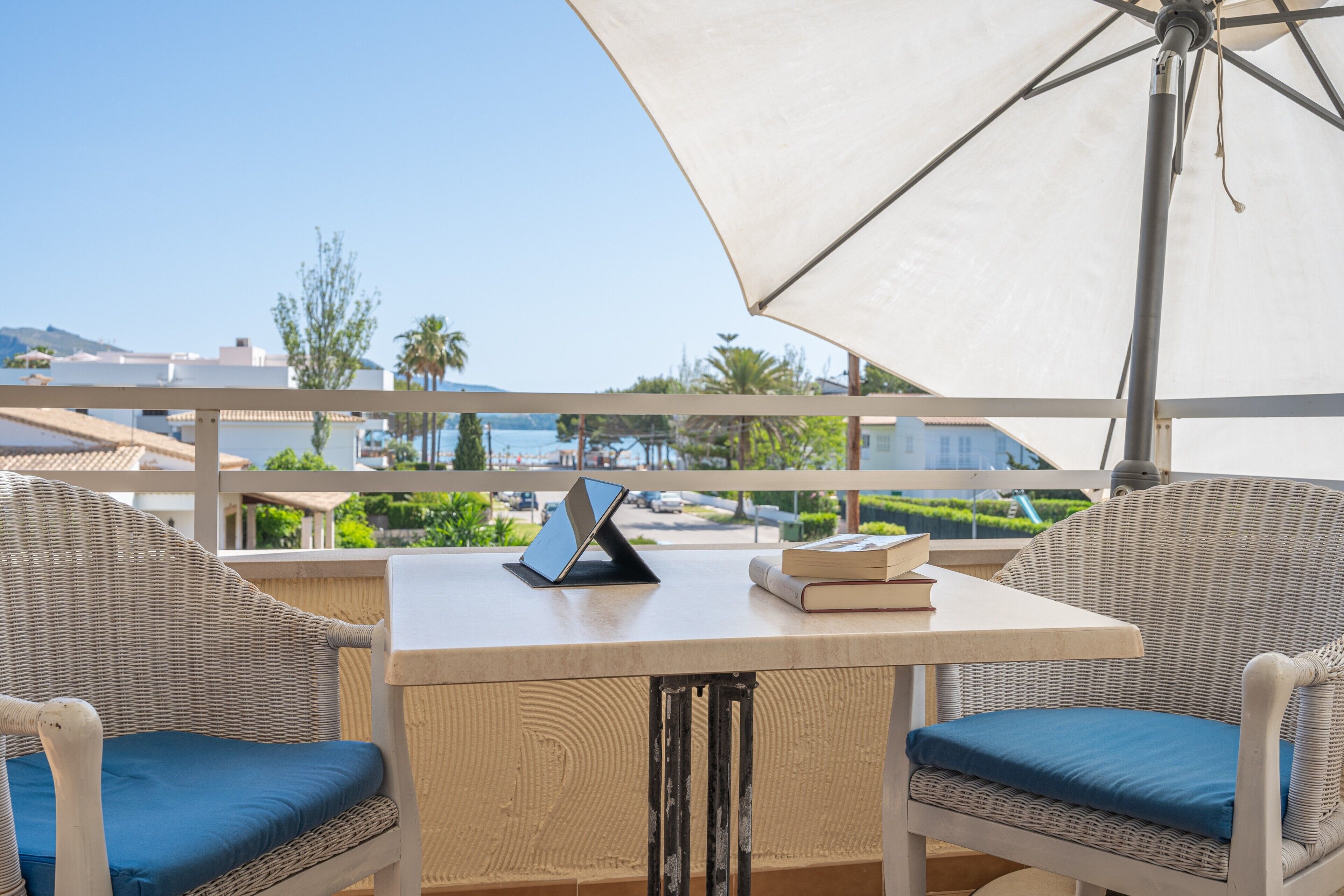 Un balcón con mobiliario de mimbre, una mesa y un parasol grande.
