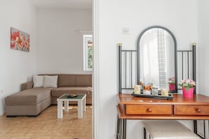 A modern living room with a sectional sofa, a small white table, and a wooden dresser with a mirror. - Apartment "Margaret House" with Wi-Fi, A/C, Terrace & Garden (Paros)