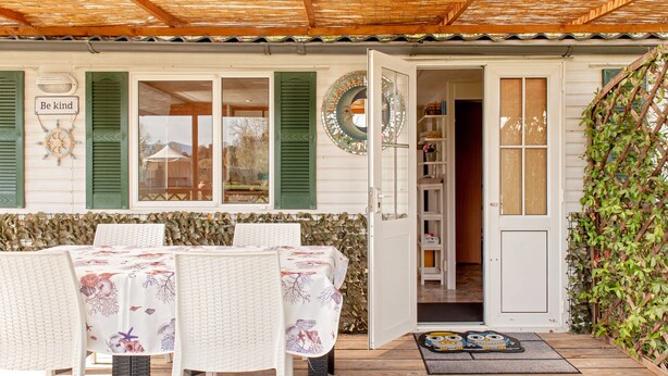 A covered patio with a table and chairs, a door leading inside, and a wall with a 'Be kind' sign.