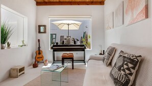 Un salón con un piano, una mesa de centro de vidrio, un sofá con cojines estampados y un techo de madera.