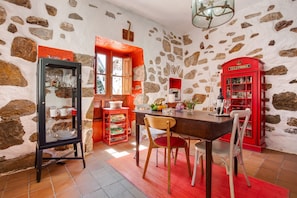 Ein Zimmer mit Steinwänden, einem Holzespeisetisch, Stühlen, einer roten Telefonzelle und einer Glasvitrine mit Geschirr.