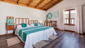 Un dormitorio con techo de madera, una cama con manta color turquesa, una mesita de noche, una pequeña mesa y una ventana con cortinas.