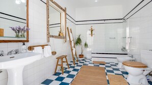 Un baño con piso a cuadros, un taburete de madera, un lavamanos, un inodoro, una bañera y un espejo.