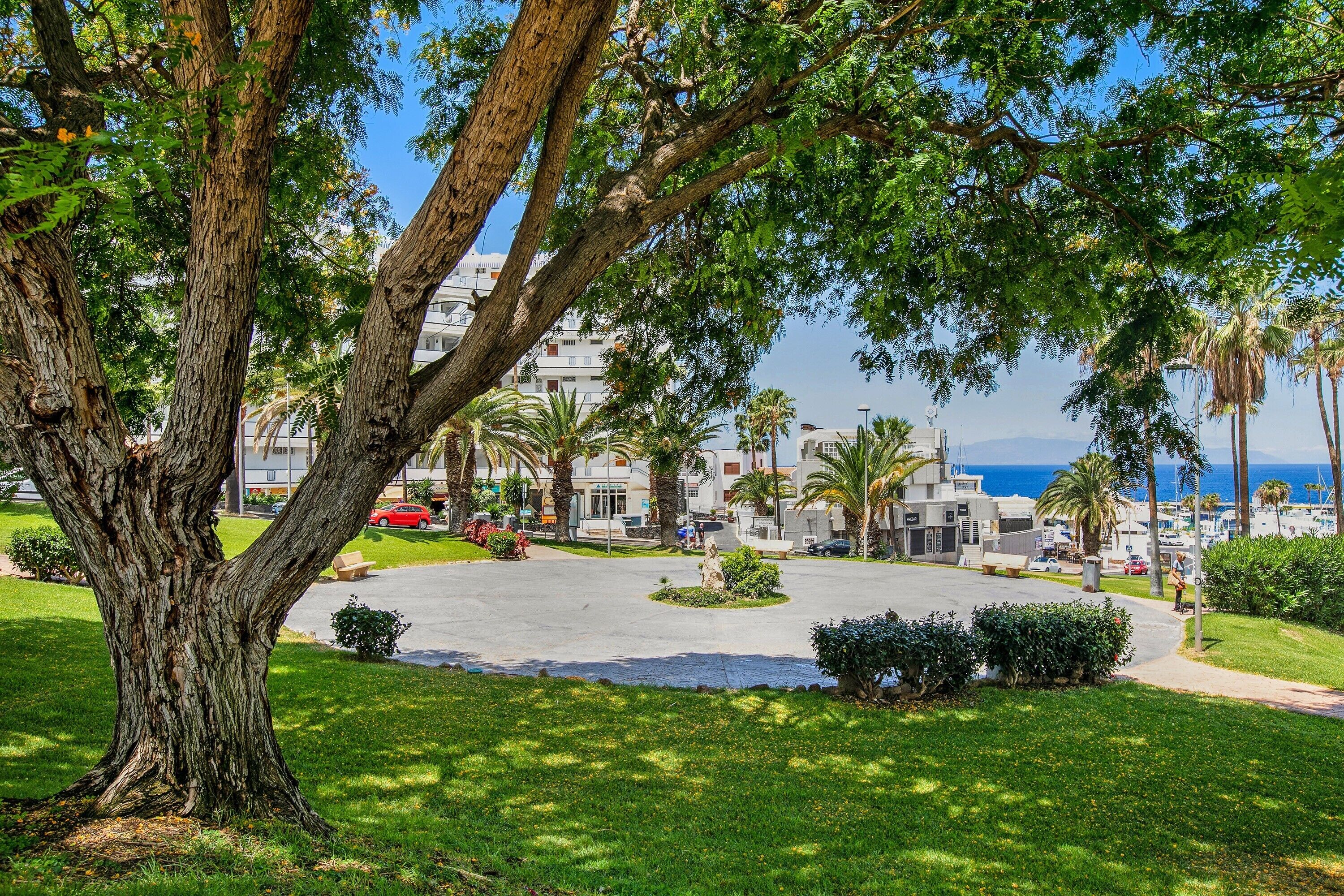 A coastal hotel with a central courtyard, palm trees, and a view of the sea.