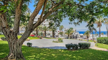 A coastal hotel with a central courtyard, palm trees, and a view of the sea.
