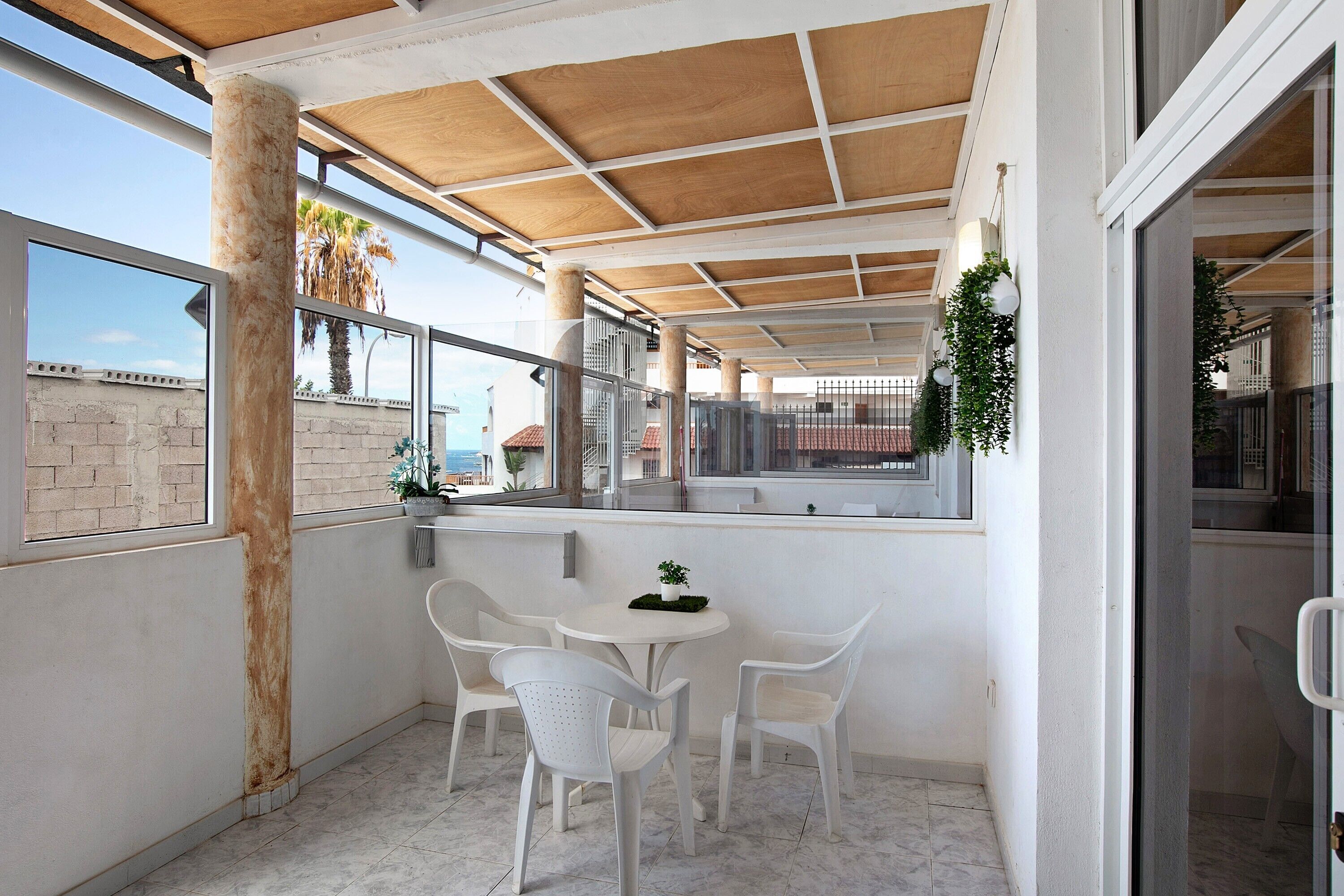 Een overdekt terras met een tafel en stoelen, uitzicht op de zee, en een balkon met planten.