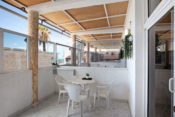 Un espace extérieur abrité, avec une table et des chaises, une vue sur la mer et un balcon agrémenté de plantes.