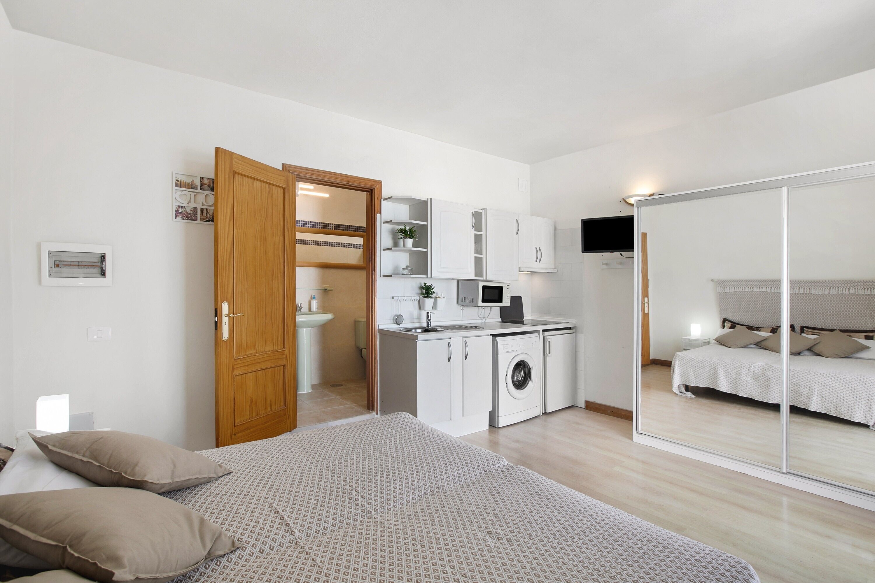 A compact bedroom with a bed, a wardrobe, and a built-in washing machine.
