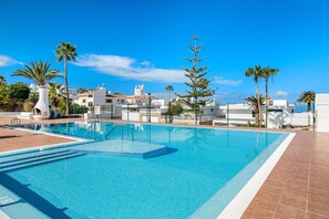 Une piscine d’un bleu éclatant, bordée d’une terrasse carrelée et entourée de palmiers et de bâtiments blancs.