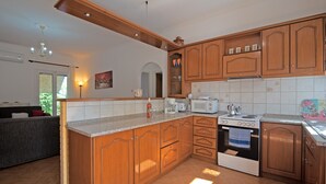 A kitchen with wooden cabinets, a microwave, an oven, and a countertop. - Apartment 'Kallithea House in Gouvia' with Mountain View, Garden & Wi-Fi (Corfu)