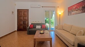 A living room with a wooden floor, a sofa, a table with candles, a door, and a painting on the wall. - Apartment 'Kallithea House in Gouvia' with Mountain View, Garden & Wi-Fi (Corfu)