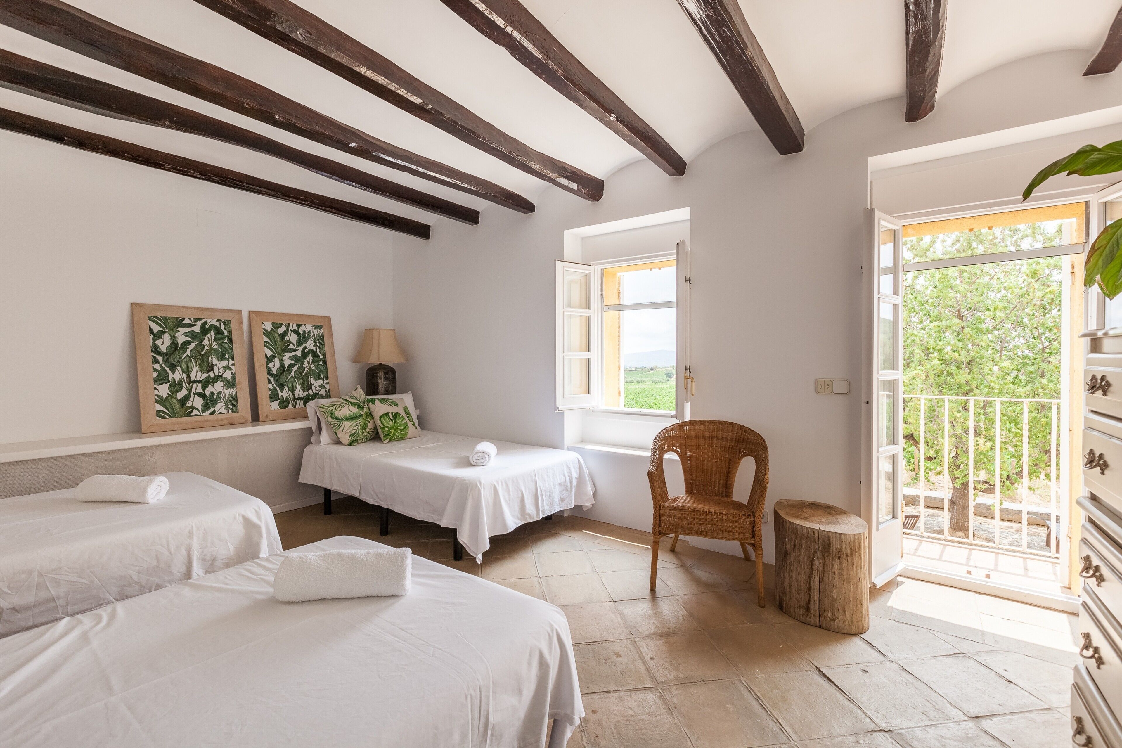 Una habitación con dos camas, una silla, una mesita y un ventanal con vistas a la vegetación.