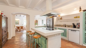 Ett kök med en köksö i mitten, barstolar, ett kylskåp och en diskmaskin.