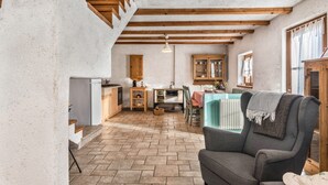 A rustic interior with exposed wooden beams, a kitchen area, and a seating area with a chair. - Chalet 'Baita Al Rossat' with Mountain Views, Garden and Wi-Fi (Sant'Orsola)