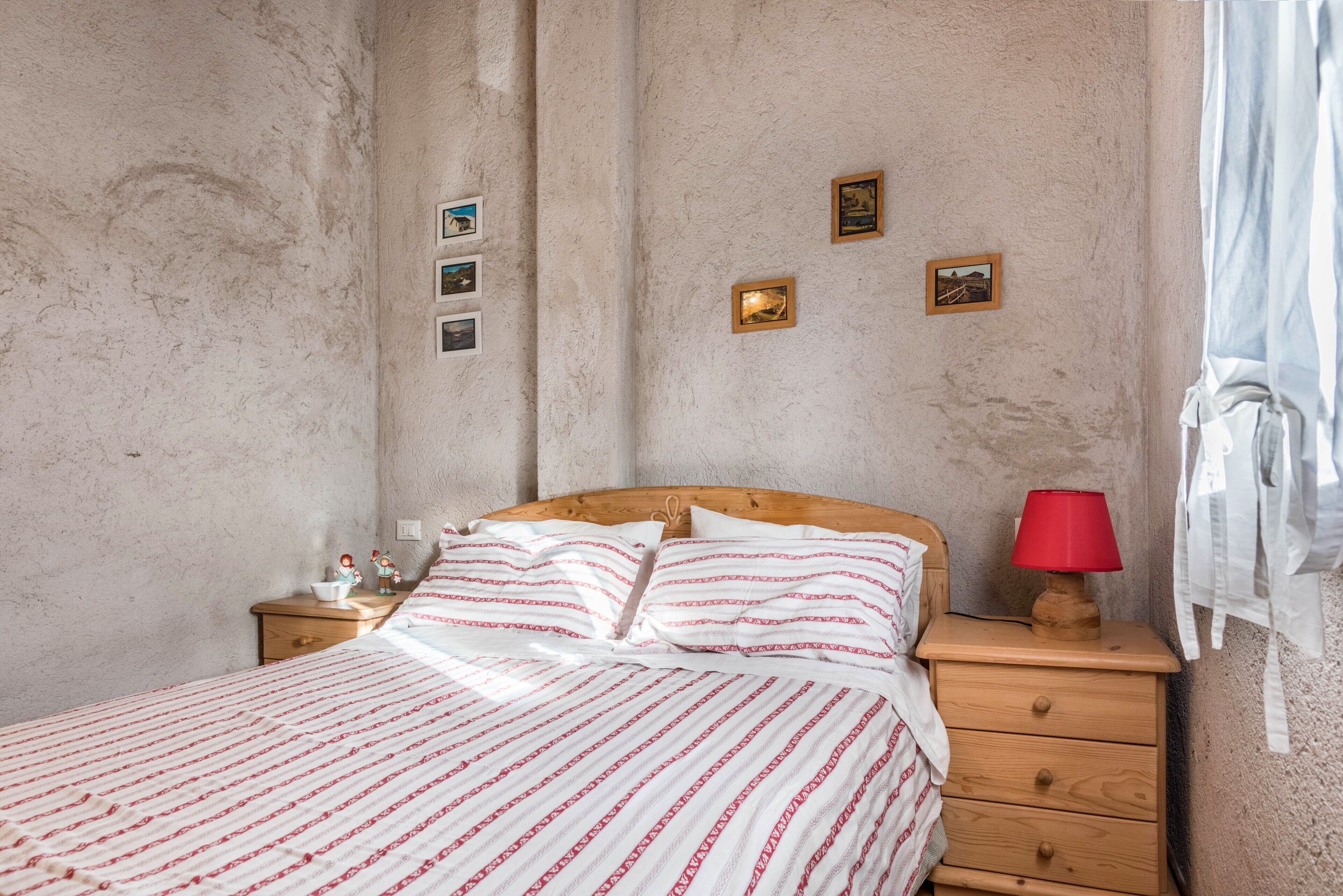 A bedroom with a bed, wooden nightstand, red lamp, and wall-mounted pictures.