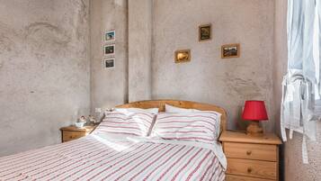 A bedroom with a bed, wooden nightstand, red lamp, and wall-mounted pictures.
