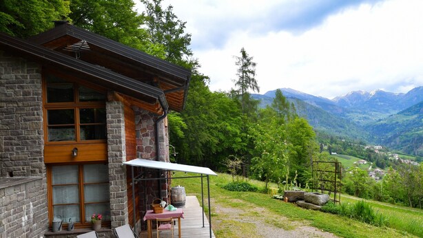 A stone building with a wooden deck, outdoor seating, and a view of a valley and mountains. - Chalet 'Baita Al Rossat' with Mountain Views, Garden and Wi-Fi (Sant'Orsola)