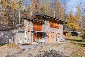 Una cabaña de piedra con terraza de madera, asientos exteriores y un porche cubierto.