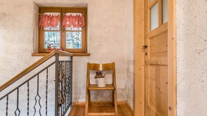 A wooden chair with a vase of flowers, a window with checkered curtains, and a wooden door. - Chalet 'Baita Al Rossat' with Mountain Views, Garden and Wi-Fi (Sant'Orsola)