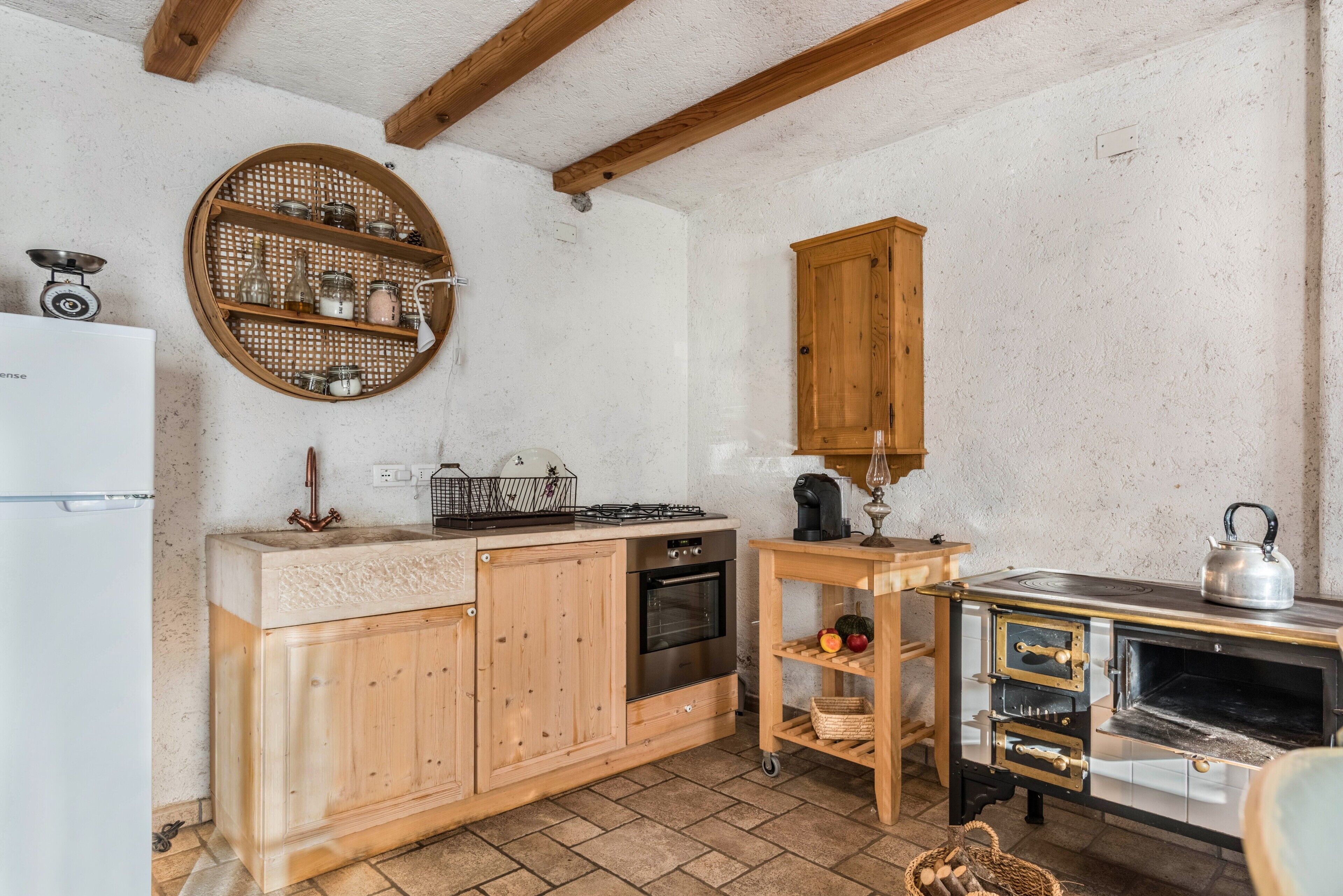 Una cocina con armarios de madera, estufa, horno, un estante redondo de mimbre y un mueble de madera.