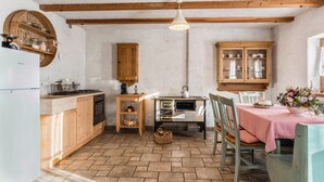 A kitchen with wooden cabinets, a dining table with a checkered tablecloth, and a hanging light fixture. - Chalet 'Baita Al Rossat' with Mountain Views, Garden and Wi-Fi (Sant'Orsola)