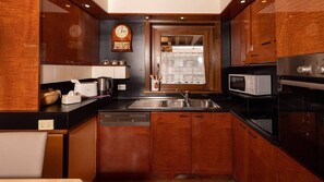 A kitchen with wooden cabinets, a stainless steel sink, a microwave, a dishwasher, and a clock on the wall.
