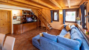 A wooden interior with a sofa, a staircase, a TV, and a kitchen area.