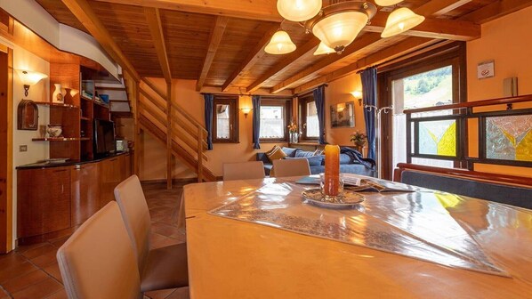 A wooden interior with a dining table, chairs, a staircase, and a view through a window.