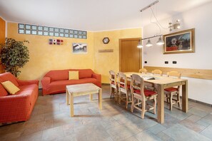 A room with a dining table, two red sofas, a wooden chair, a potted plant, a clock, and a framed picture on the wall.