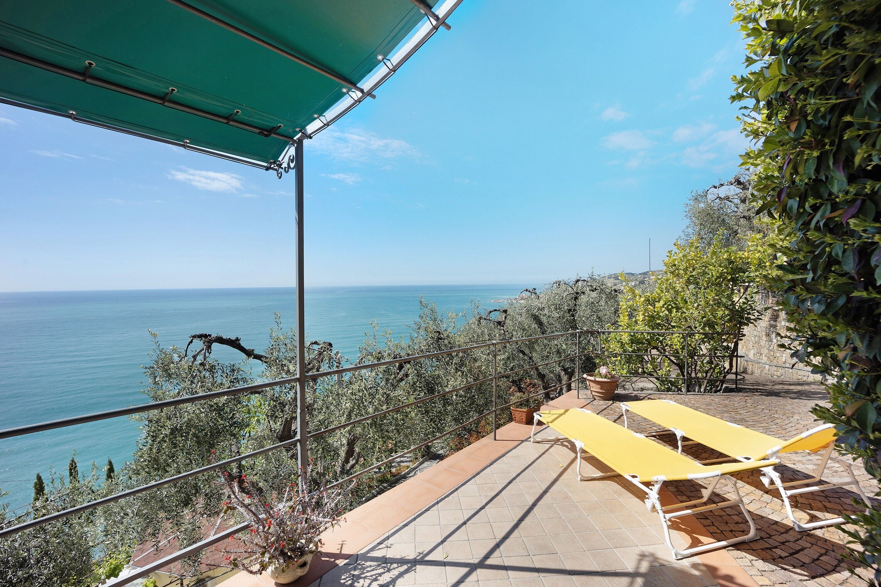 A balcony with a view of the sea, a yellow table, and a potted plant.