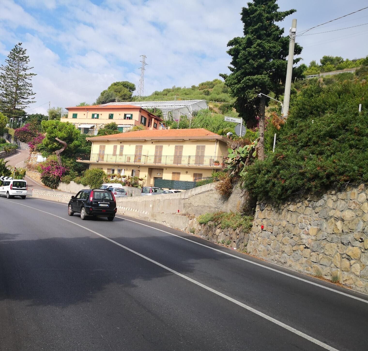 A road with cars, a stone wall, and buildings with balconies.