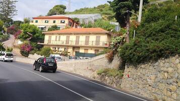 A road with cars, a stone wall, and buildings with balconies.