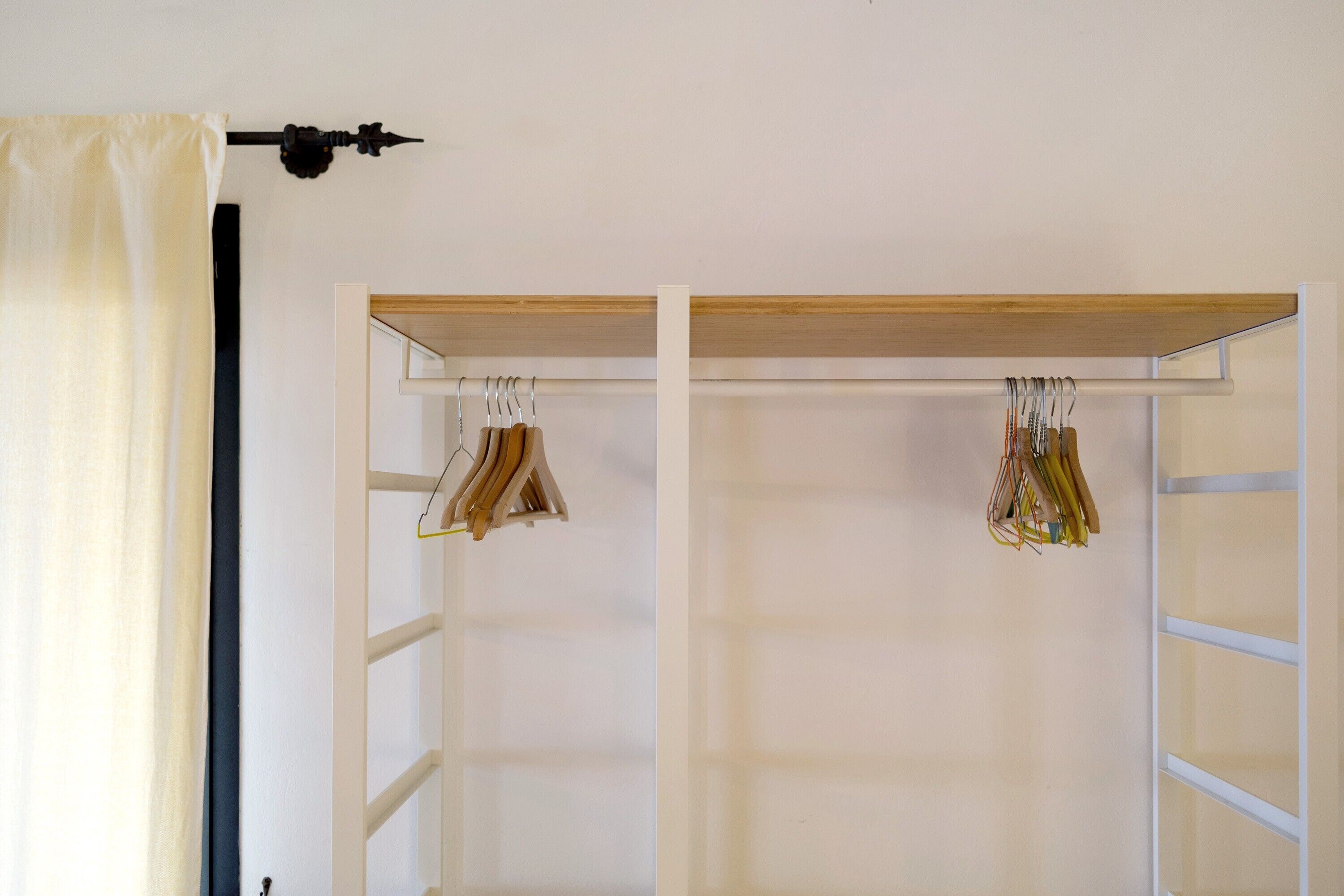 Ein Zimmer mit einem weißen Kleiderschrank, einer Holztrennwand und einer schwarzen Wandleuchte.