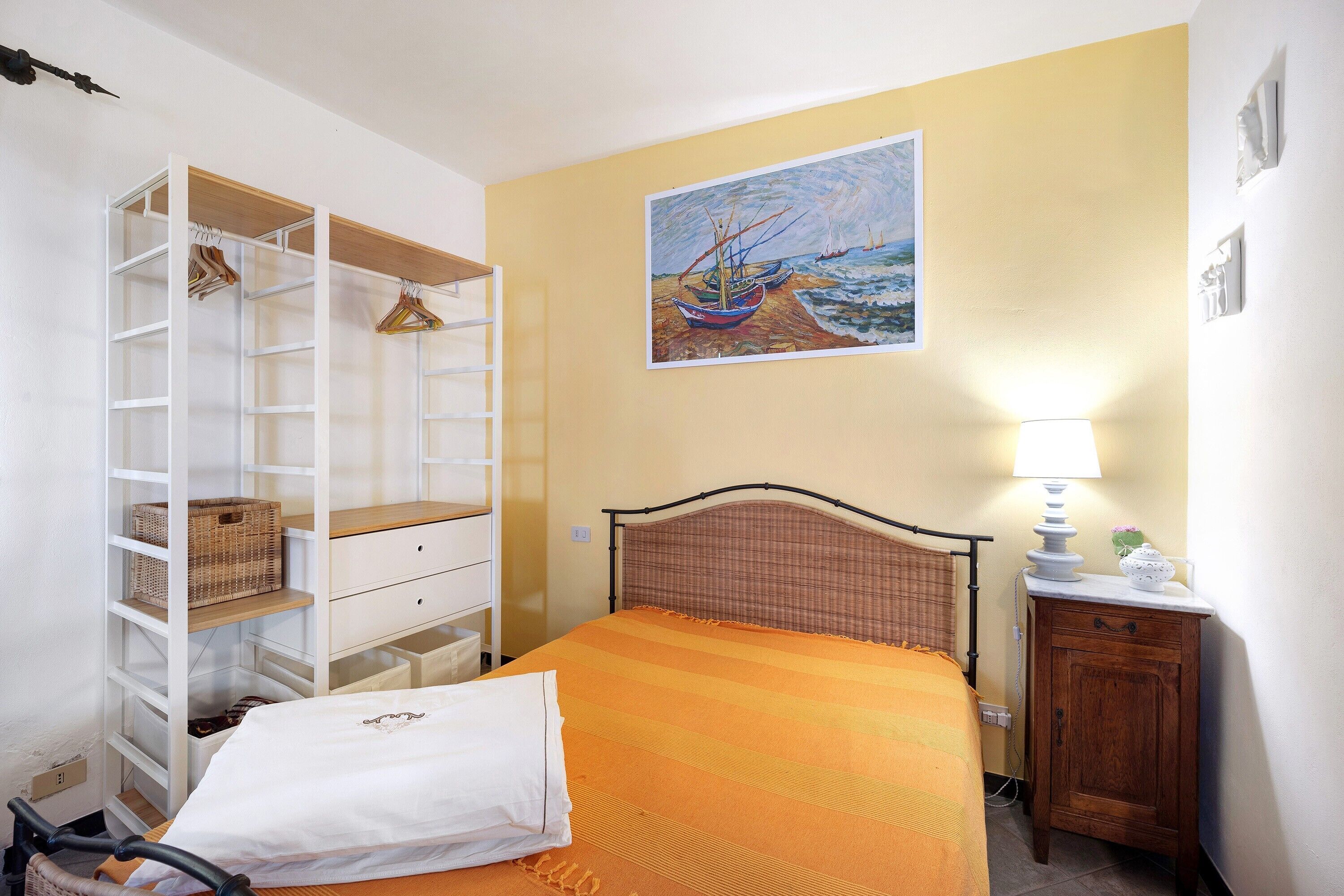Une chambre à coucher comprenant un lit, une table de chevet, une lampe, un tableau, une armoire et une chaise.