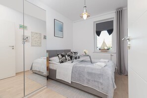 Un dormitorio moderno con cama, mesitas de noche, ventana con cortinas y obras de arte en las paredes.
