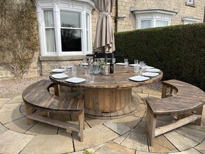 Une table ronde en bois, prévue pour six personnes, avec des bancs assortis, le tout entouré de carreaux de pierre.