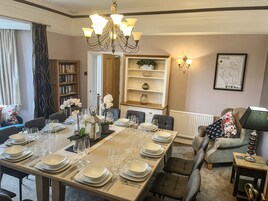 A dining room with a long table set for six, a chandelier, a bookshelf, and a map on the wall.