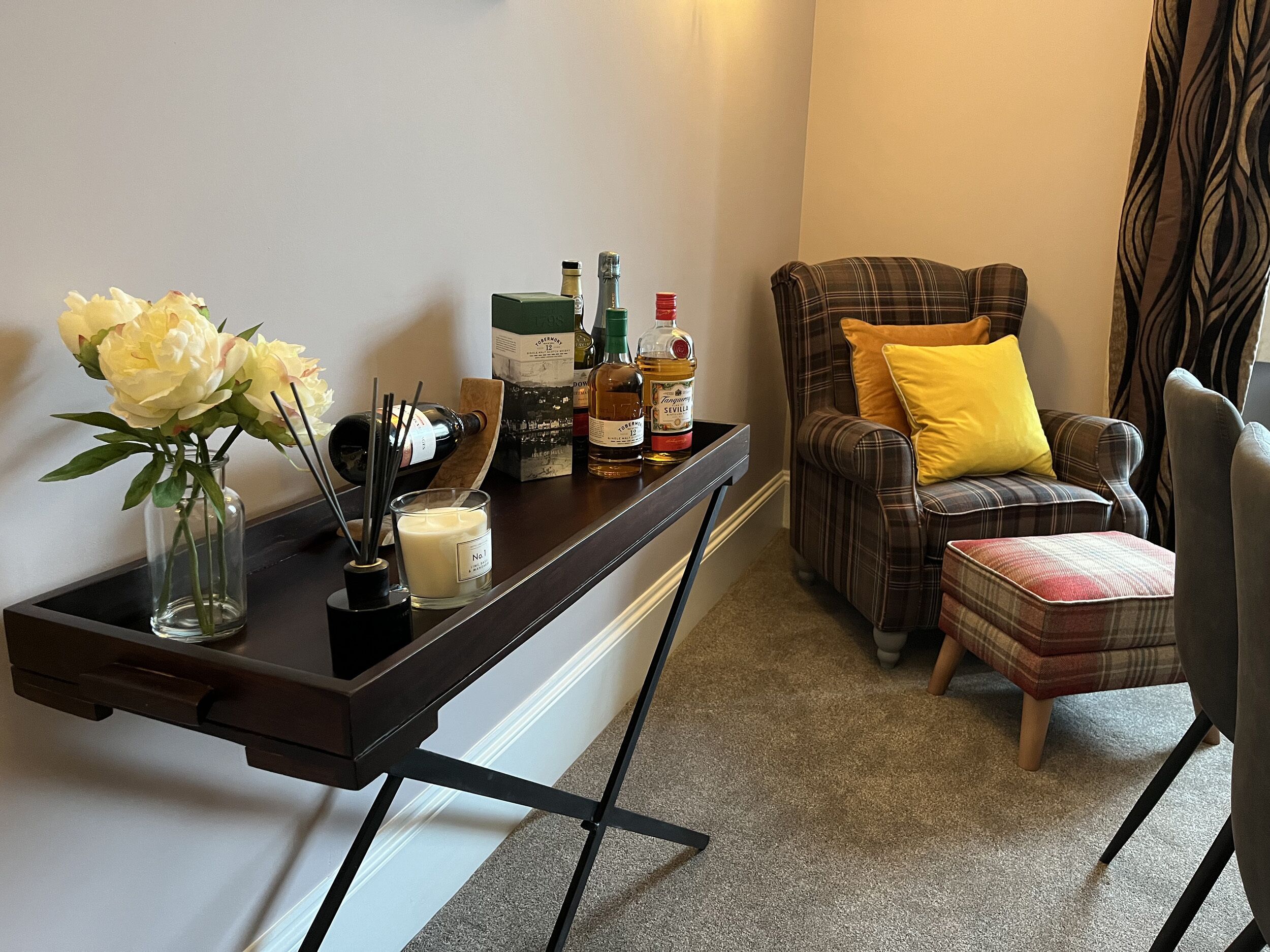 A corner of a room with a dark wooden desk, a chair with a plaid cushion, and a small ottoman.