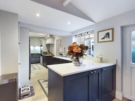 A modern kitchen with a central island, a dining area, and a view of the garden through the window.