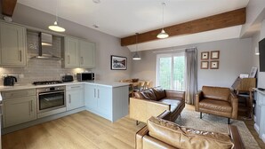 Una cocina moderna con zona de comedor, que cuenta con un ventanal grande, vigas de madera y un sofá de cuero.