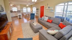 A spacious living room with a grey sofa set, a wooden entertainment center, and a dining area with a red door. - Bikini Bottom: Close to pool, dining, beach, pets (Galveston)