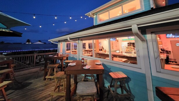 An outdoor dining area with wooden tables and chairs, string lights, and a view of the ocean. - Bikini Bottom: Close to pool, dining, beach, pets (Galveston)