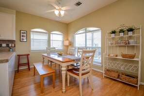 A dining area with a wooden table, chairs, and a white shelf with baskets.