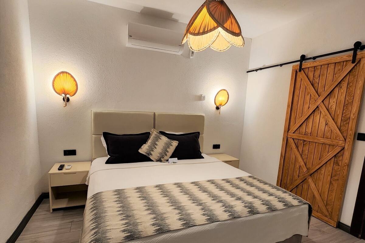 Un dormitorio con una cama grande, dos lámparas de noche, un ventilador de techo y una puerta de madera.
