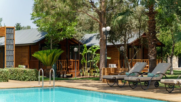 A pool area with lounge chairs and wooden cabins in the background. - Dolce Vita Luxury Bungalows (Bodrum)