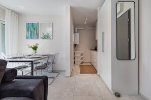 A modern kitchen with white cabinets, a dining area with a table and chairs, and a hallway leading to a bathroom.
