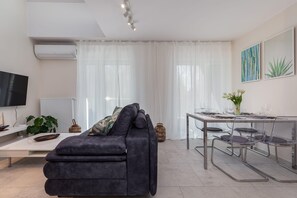 A modern living room with a dark sofa, a dining table with chairs, a TV, and a radiator.